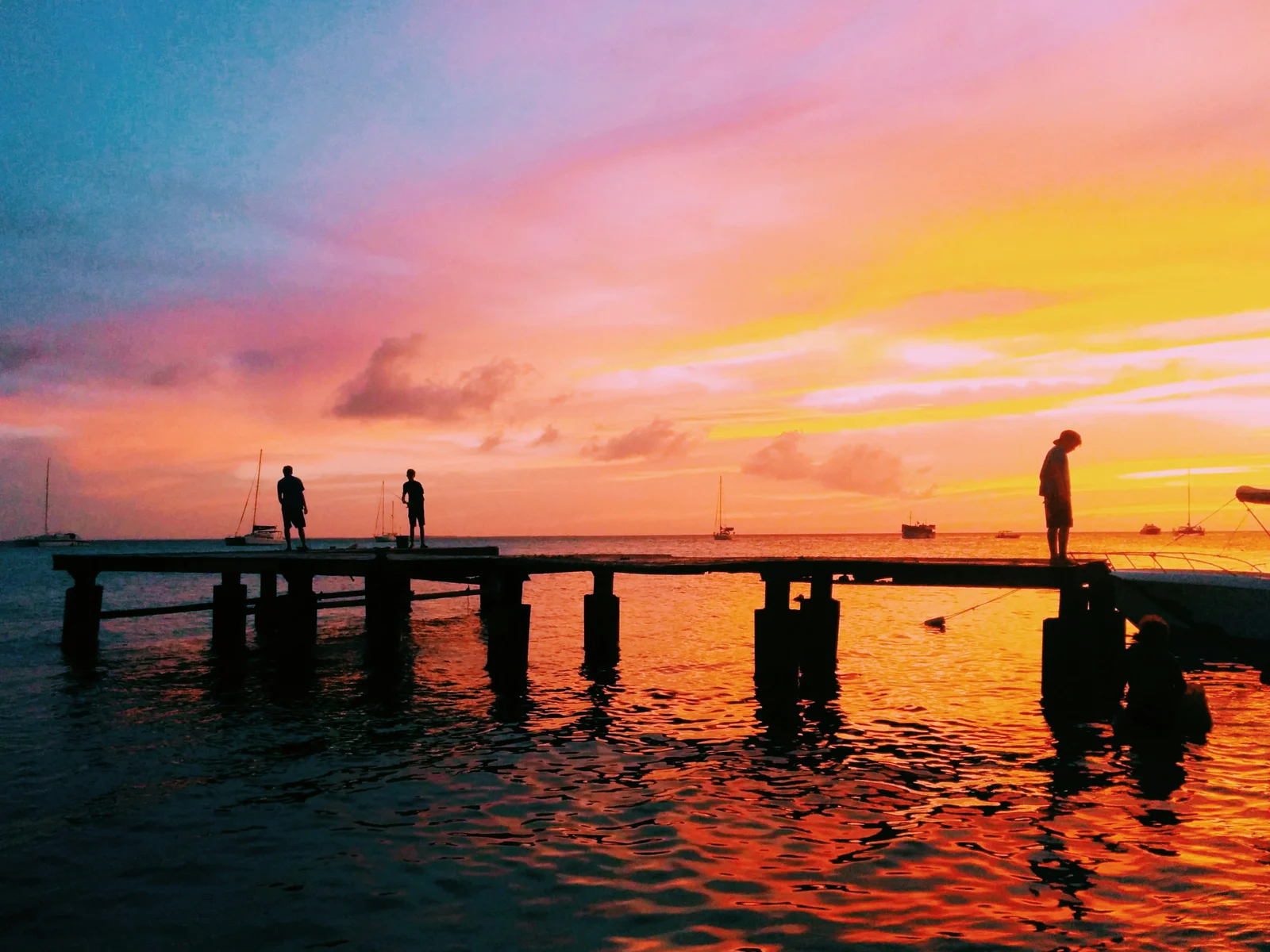 Trois amis en silhouette sur une jetée au coucher de soleil, silhouettes observant la mer dorée