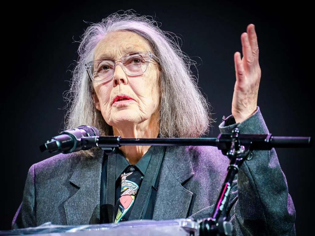 Portrait de la poétesse Anne Carson au pupitre, lunettes transparentes et cravate colorée, aux National Book Awards 2024