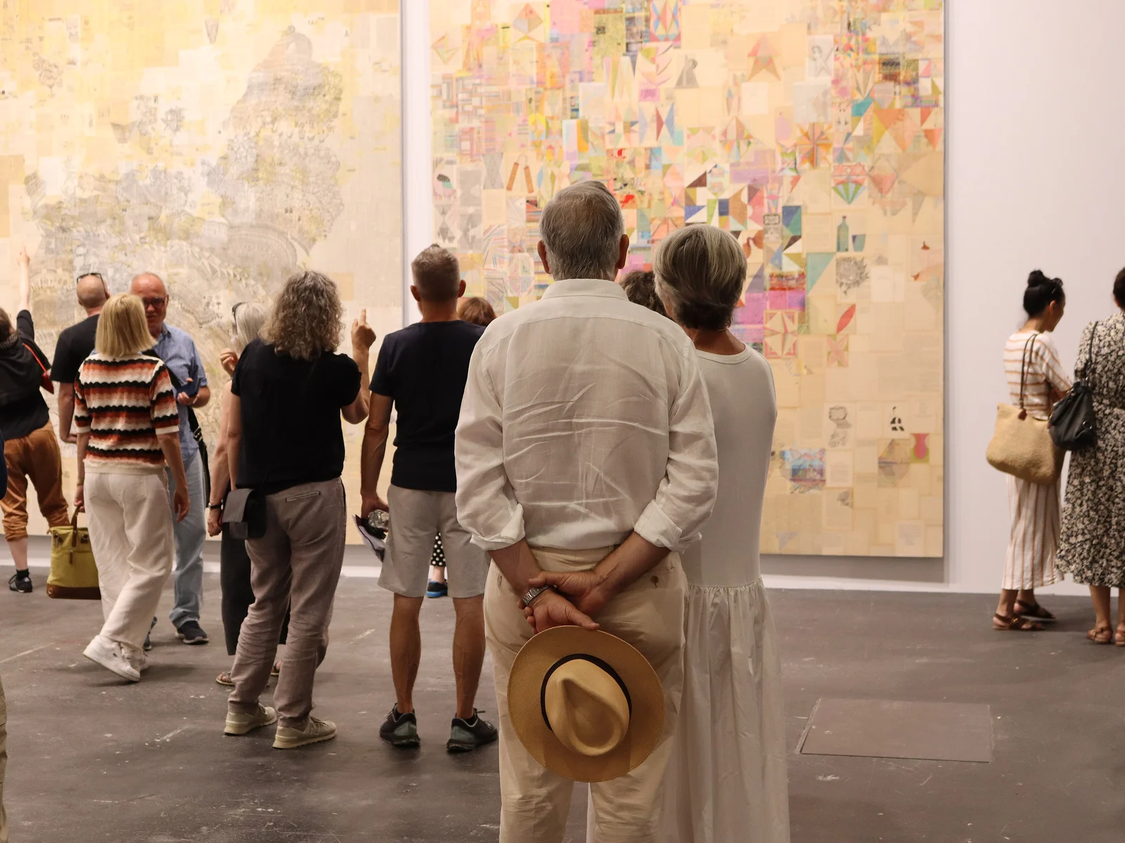 Visiteurs devant une toile monumentale en collage dans la section Unlimited d'Art Basel 2025 à Bâle, de dos, chapeau en main