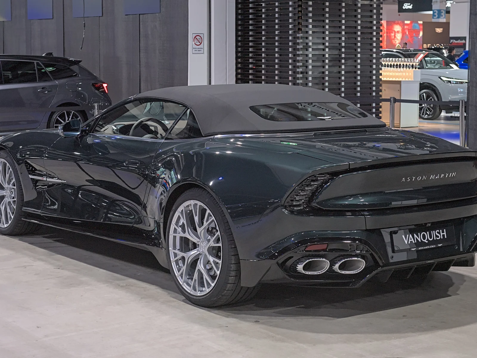Aston Martin Vanquish Volante vert sombre, toit en toile fermé, vue de trois quarts arrière au salon Auto Zürich 2025