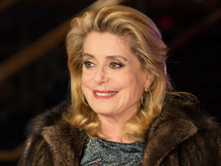 Catherine Deneuve souriante en manteau de fourrure, cheveux blonds et rouge à lèvres, au Festival de Berlin 2017