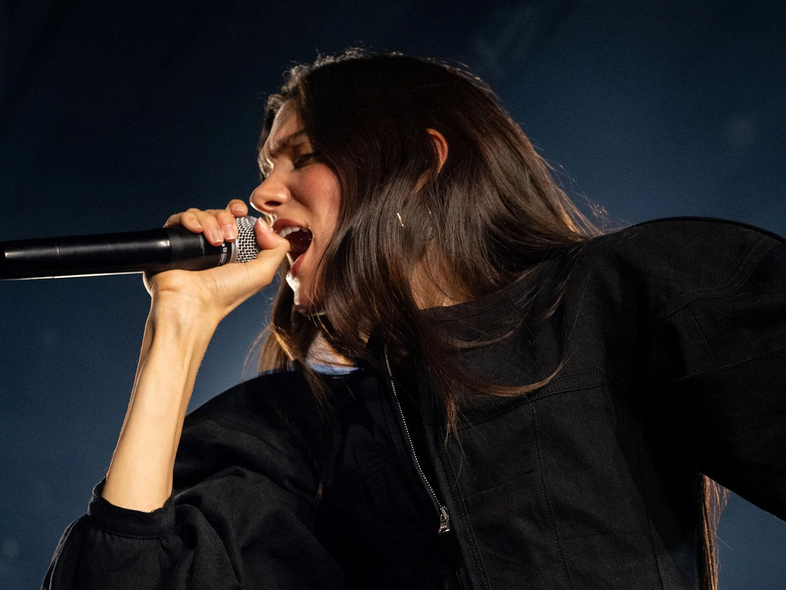 Gros plan sur Charlotte Cardin, cheveux longs et combinaison noire, micro à la main, en plein concert à Montreux en 2026