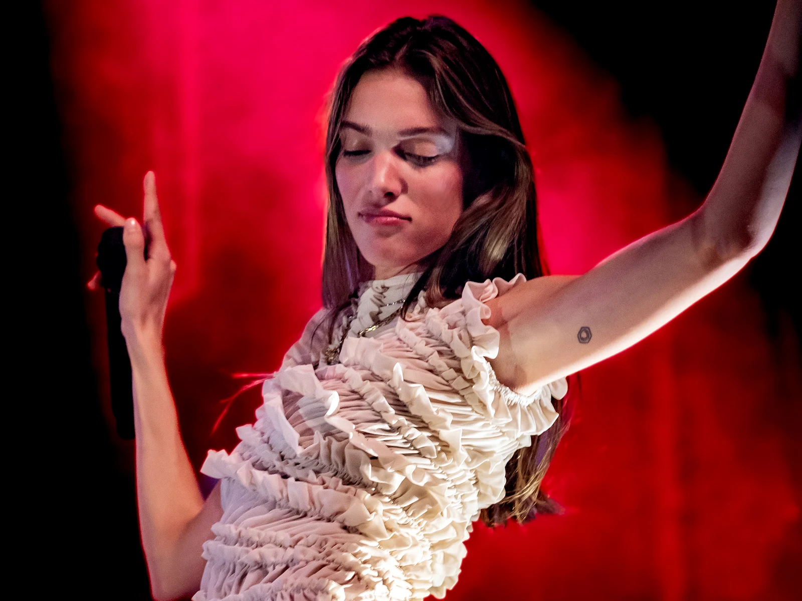 Charlotte Cardin en haut à volants dans une lumière rouge, le bras levé, micro en main, à l'El Rey de Los Angeles