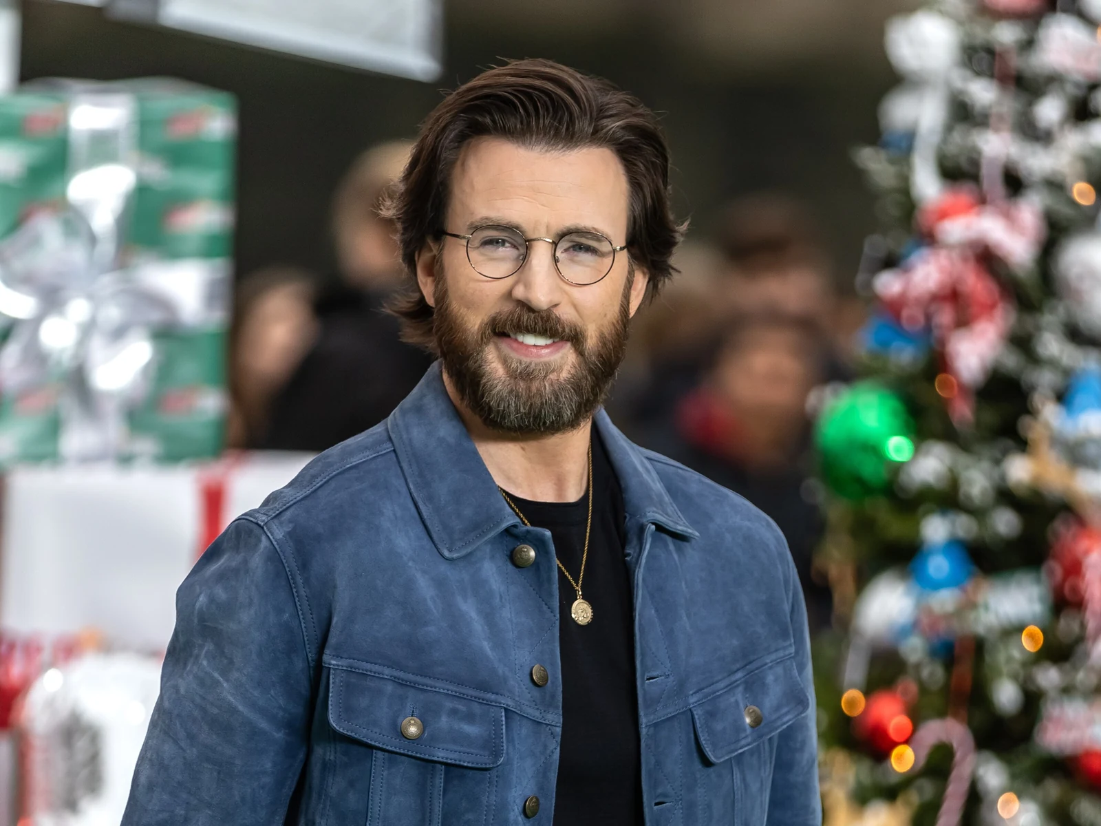 Chris Evans, barbe et lunettes rondes, sourit en veste de daim bleu à l'avant-première de Red One en 2024