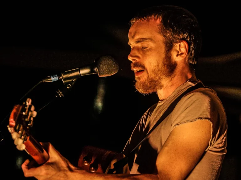 Damien Rice chante et joue de la guitare acoustique dans une lumière chaude, showcase à Paris en 2014