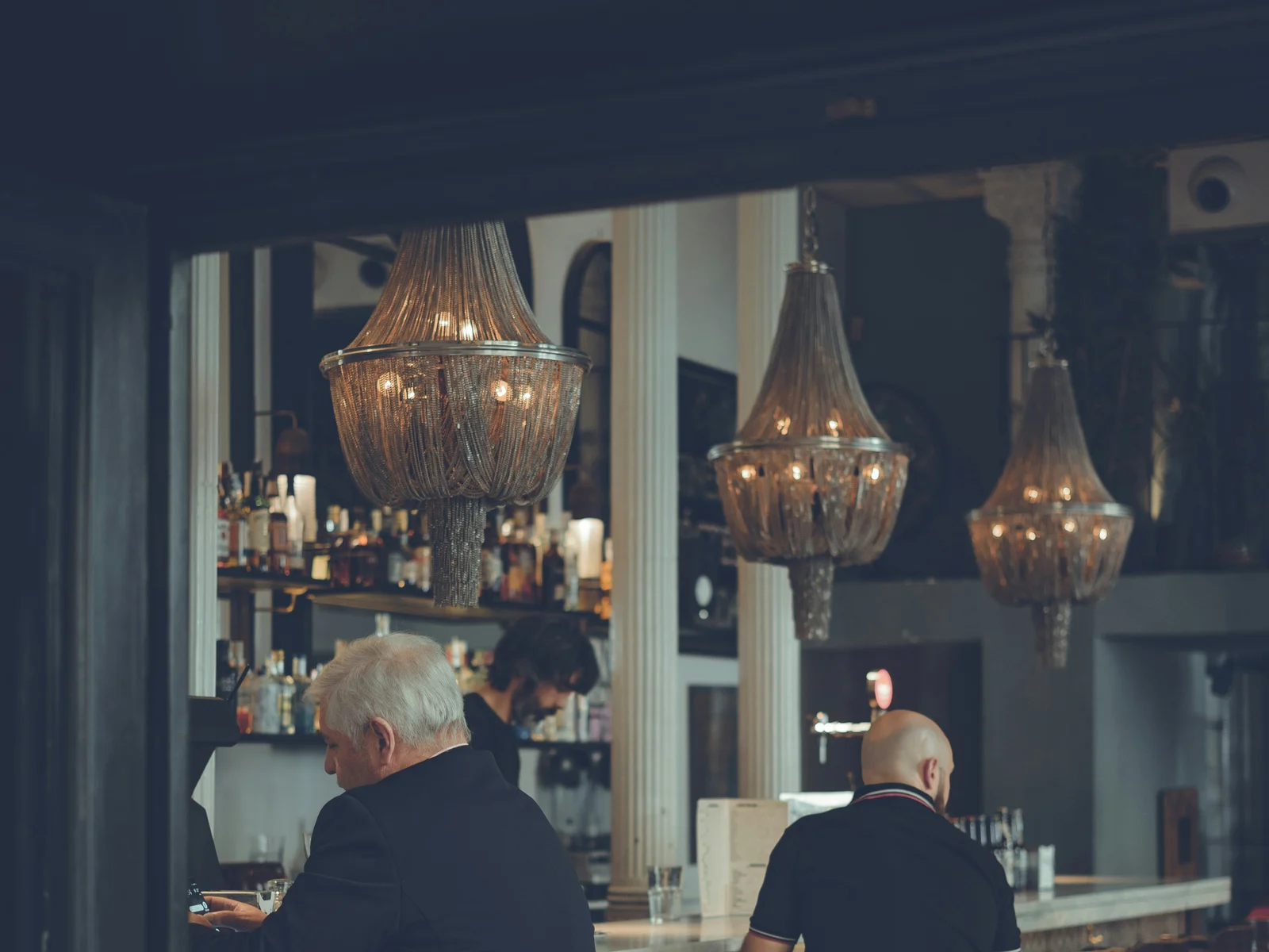 Deux hommes assis au comptoir d'un bar élégant, conversation intime avec éclairage doré des lustres