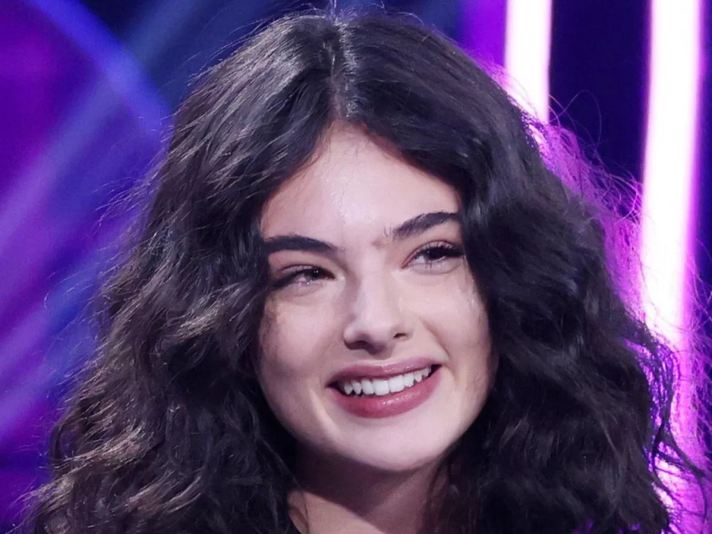 Portrait souriant de Deva Cassel, cheveux bruns bouclés et blouse noire ajourée, sur un plateau télé à Milan en 2025
