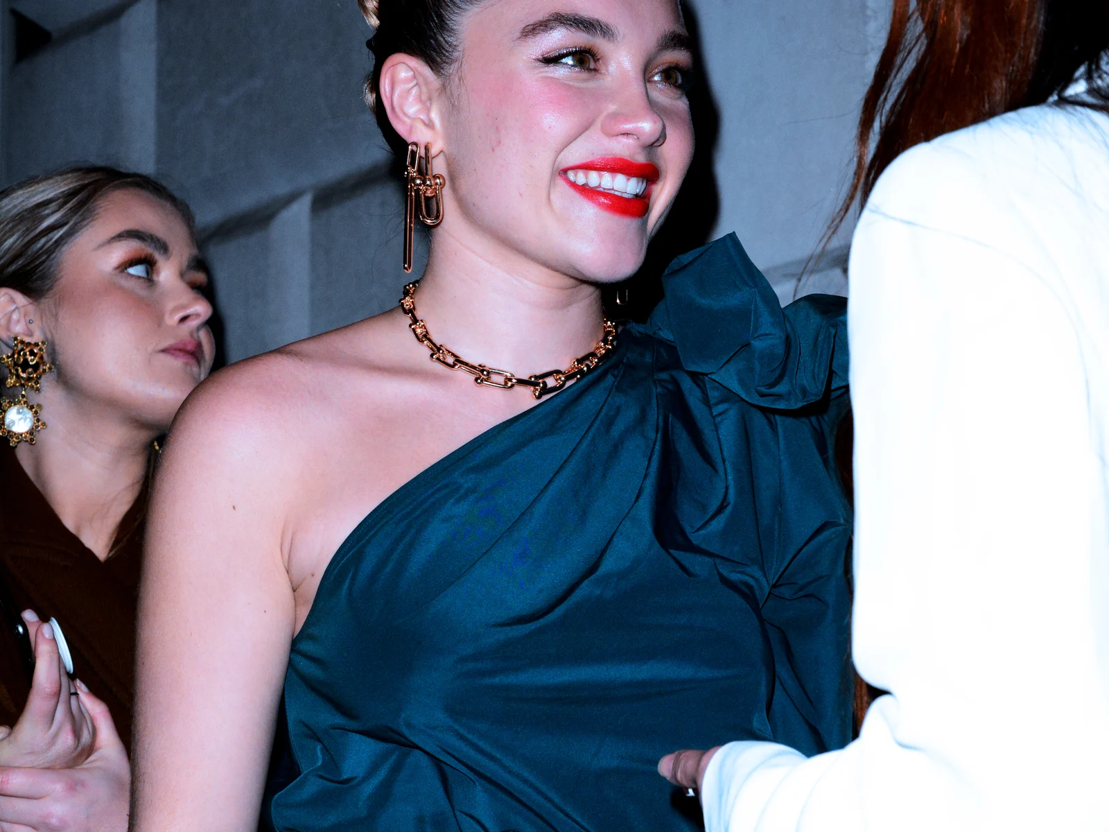 Florence Pugh en robe de soirée bleu-vert et collier en chaîne dorée, souriante lors d'une fête à Londres en 2020