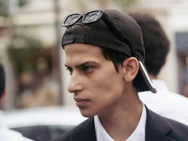 Portrait de profil d'un jeune homme en blazer noir et chemise blanche, casquette portée à l'envers, Paris Fashion Week