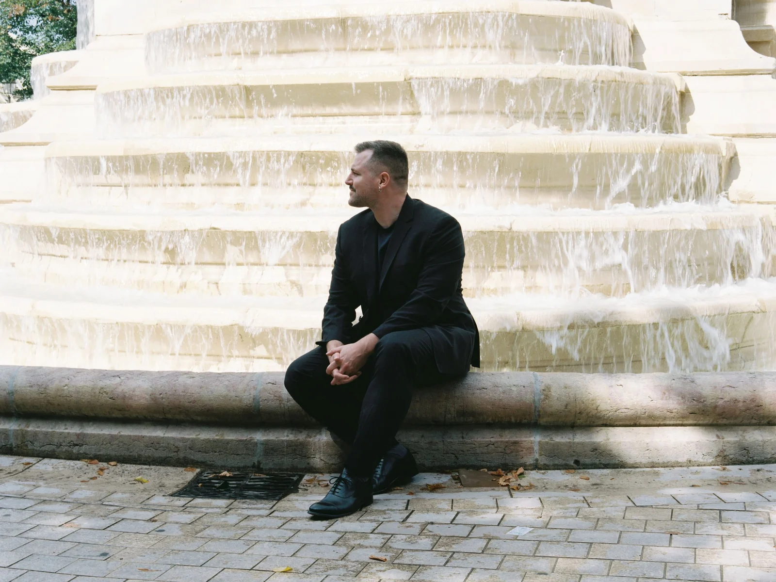 Karim Crippa, directeur d'Art Basel Paris 2026, assis au bord d'une fontaine parisienne, portrait officiel pour Art Basel