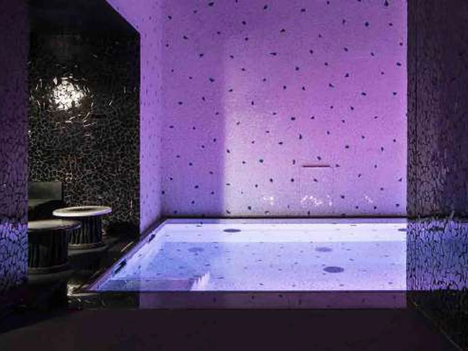 Piscine intérieure des Bains à Paris, éclairée de violet, aux murs de mosaïque sombre