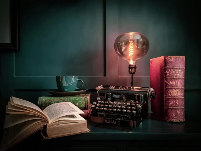 Machine à écrire ancienne, livre ouvert et ampoule à filament sur fond vert sombre, illustration des prix littéraires
