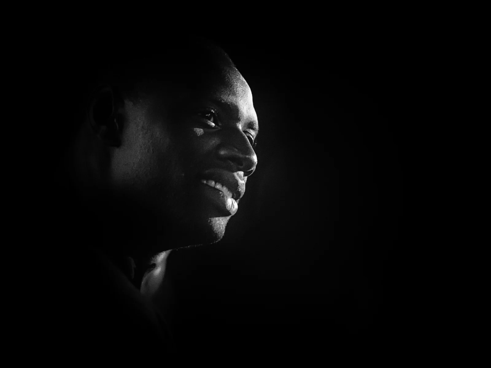 Portrait noir et blanc en clair-obscur d'Omar Sy souriant de profil, avant-première de Samba, Le Mans, octobre 2014