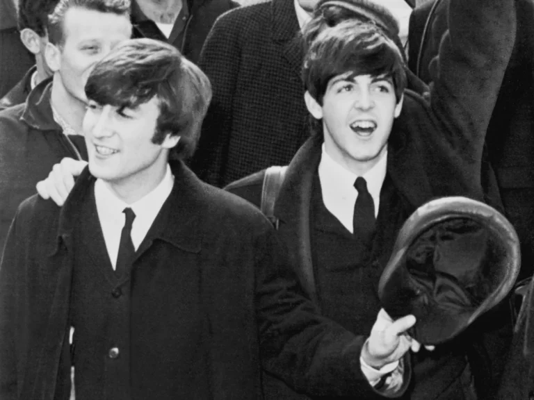 Paul McCartney, rieur et casquette à la main, aux côtés de John Lennon à l'aéroport Kennedy de New York en 1964