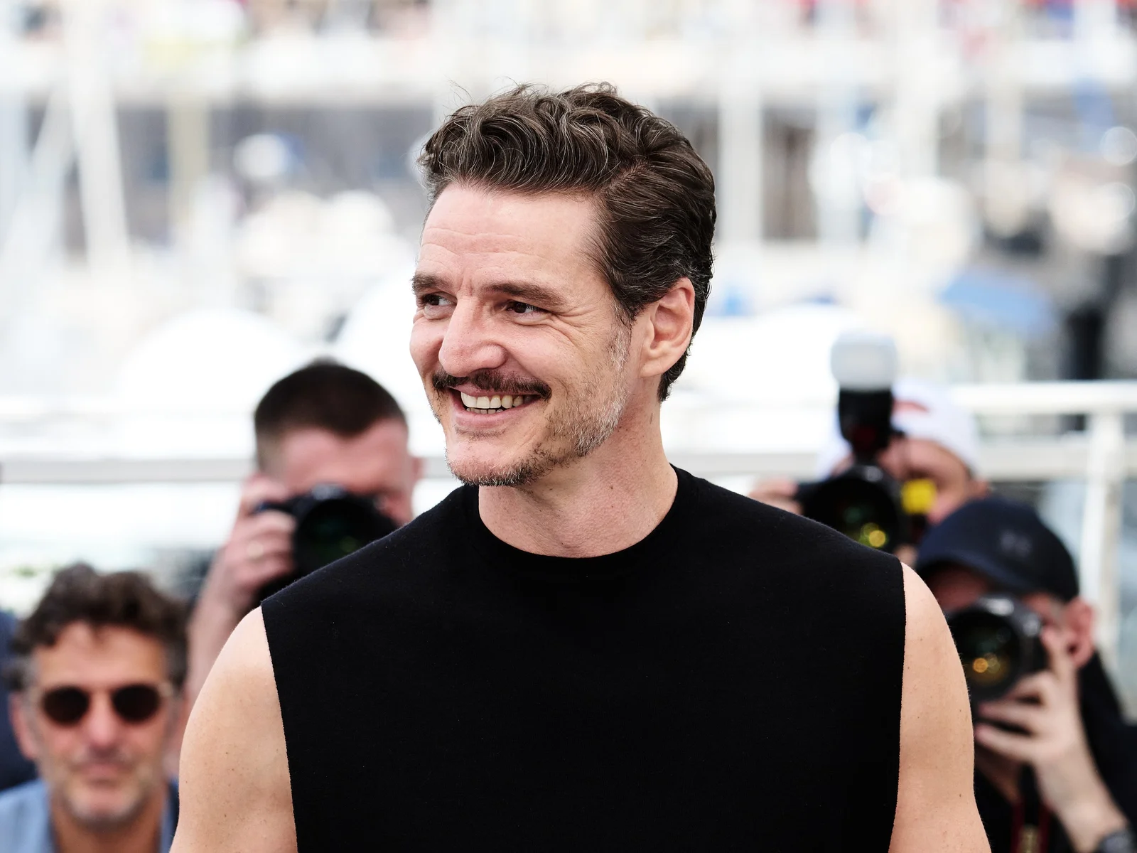 Pedro Pascal rieur, en haut noir sans manches, devant les photographes au photocall du Festival de Cannes 2025