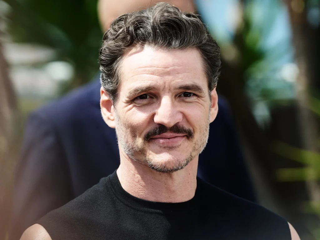 Portrait de l'acteur Pedro Pascal souriant, cheveux bruns et moustache, au photocall du Festival de Cannes 2025