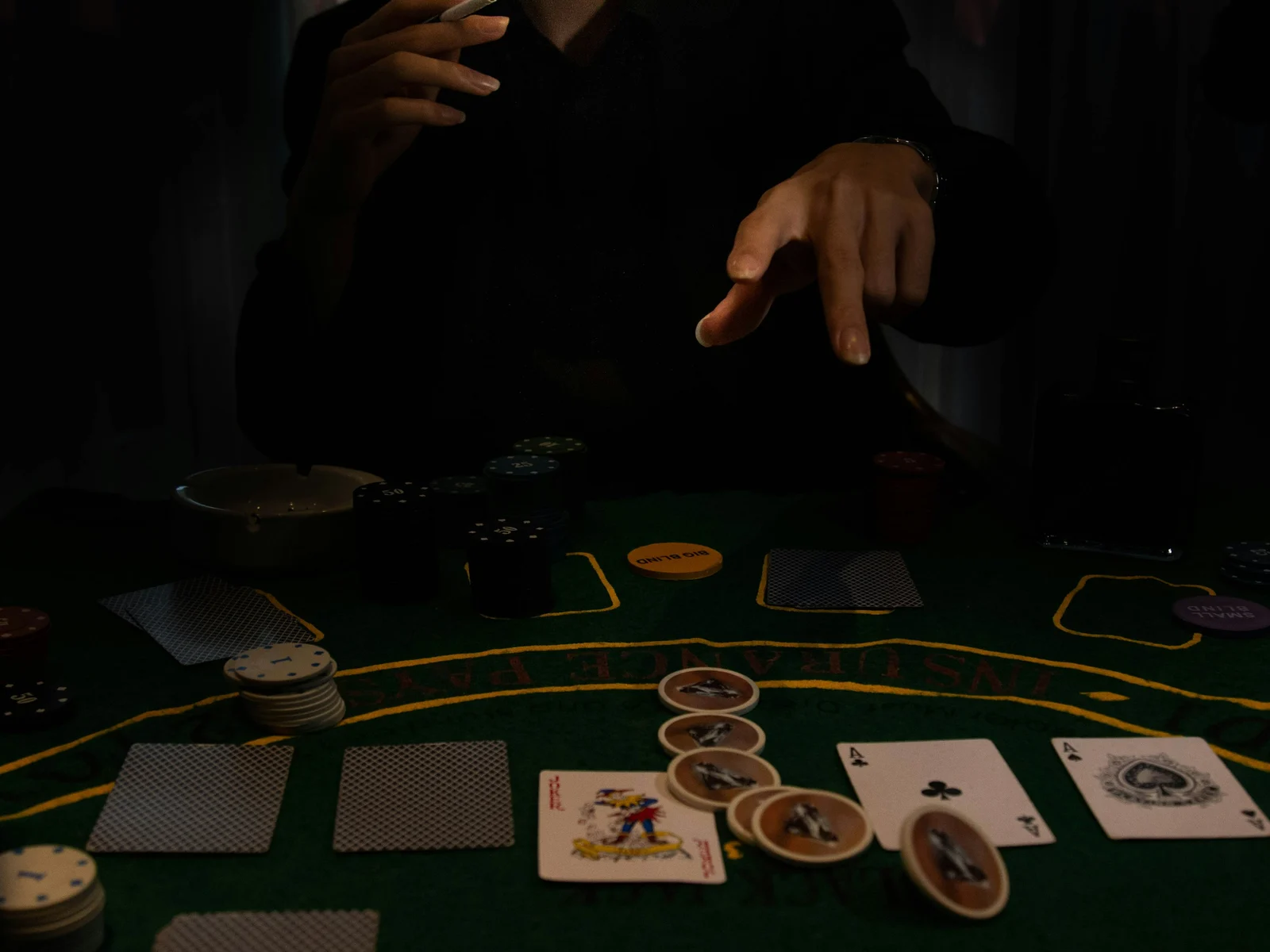 Table de poker sous une lumière tamisée : main d'un joueur au-dessus des cartes et jetons empilés sur le feutre vert