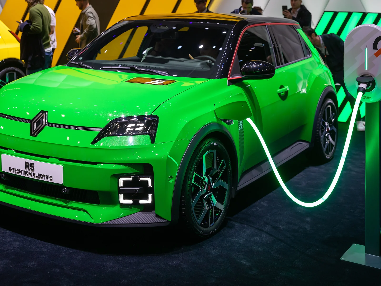Renault 5 E-Tech électrique verte branchée à une borne de recharge lumineuse au Salon de Genève 2024