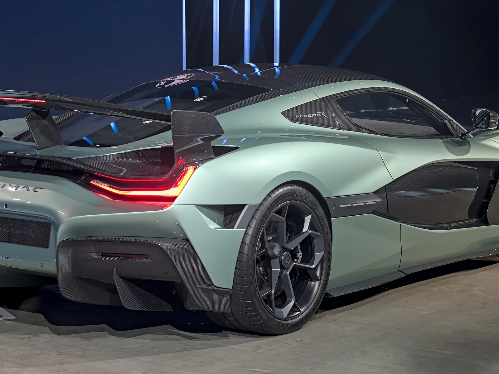 Arrière de l'hypercar électrique Rimac Nevera R, vert sauge et carbone, feux rouges allumés dans un décor sombre