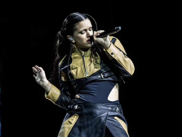 Rosalía en concert au Movistar Arena de Santiago, micro à la main, yeux fermés, veste de cuir noir et ocre