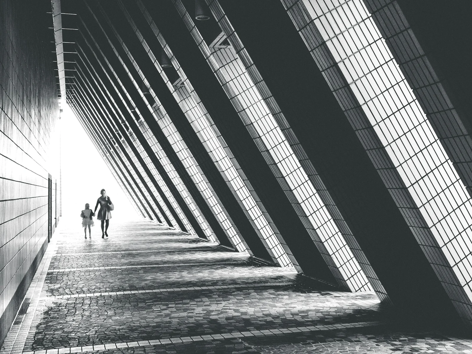 Deux silhouettes marchent dans un couloir aux lignes géométriques, entre ombres et lumière, comme dans un film d'espionnage