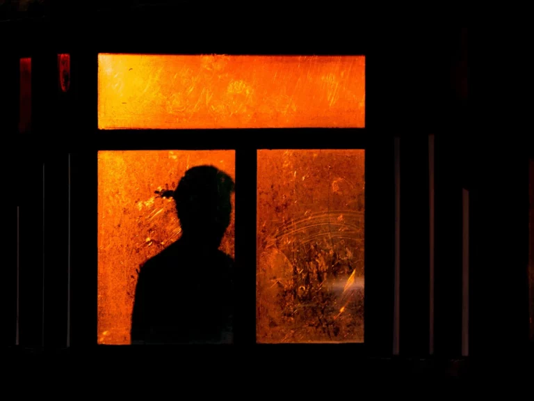 Silhouette d'un homme seul derrière une vitre embuée éclairée d'une lumière orange chaude, ambiance film noir nocturne