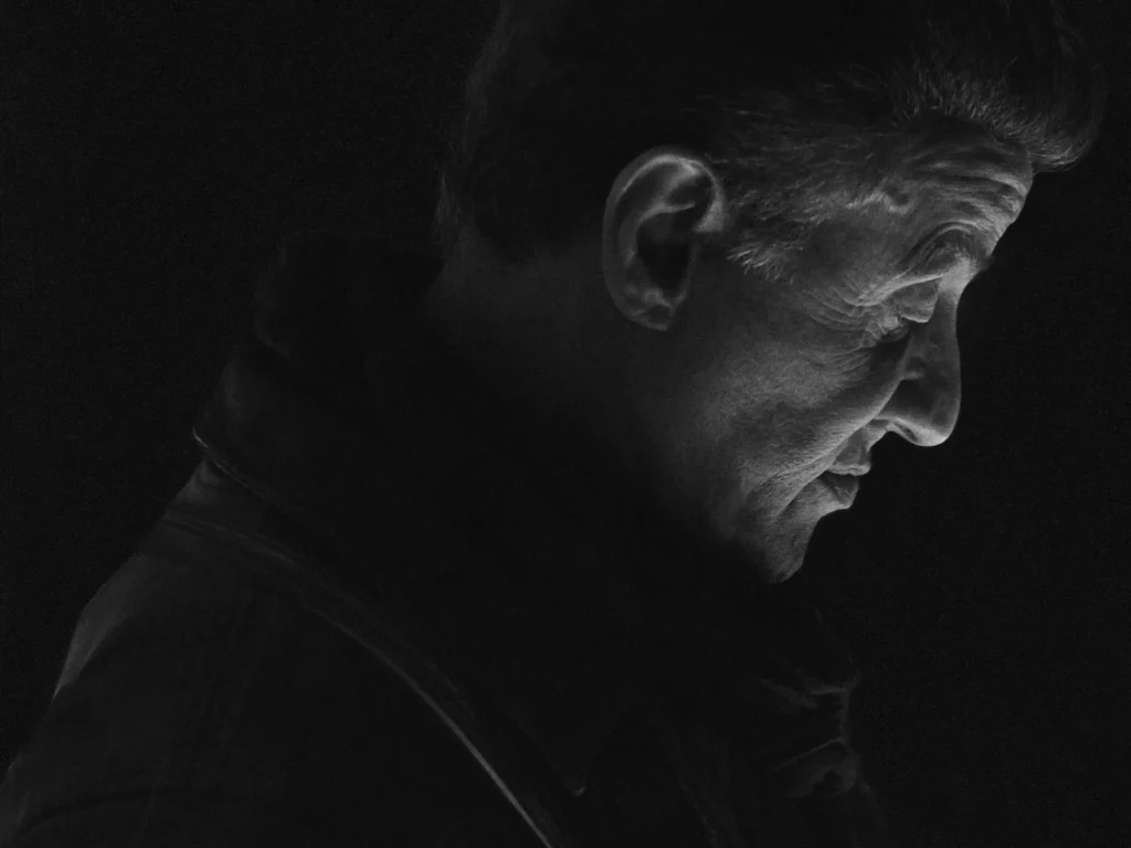 Profil de Sylvester Stallone en noir et blanc, visage baissé émergeant de l'ombre, éclairage dramatique de clair-obscur