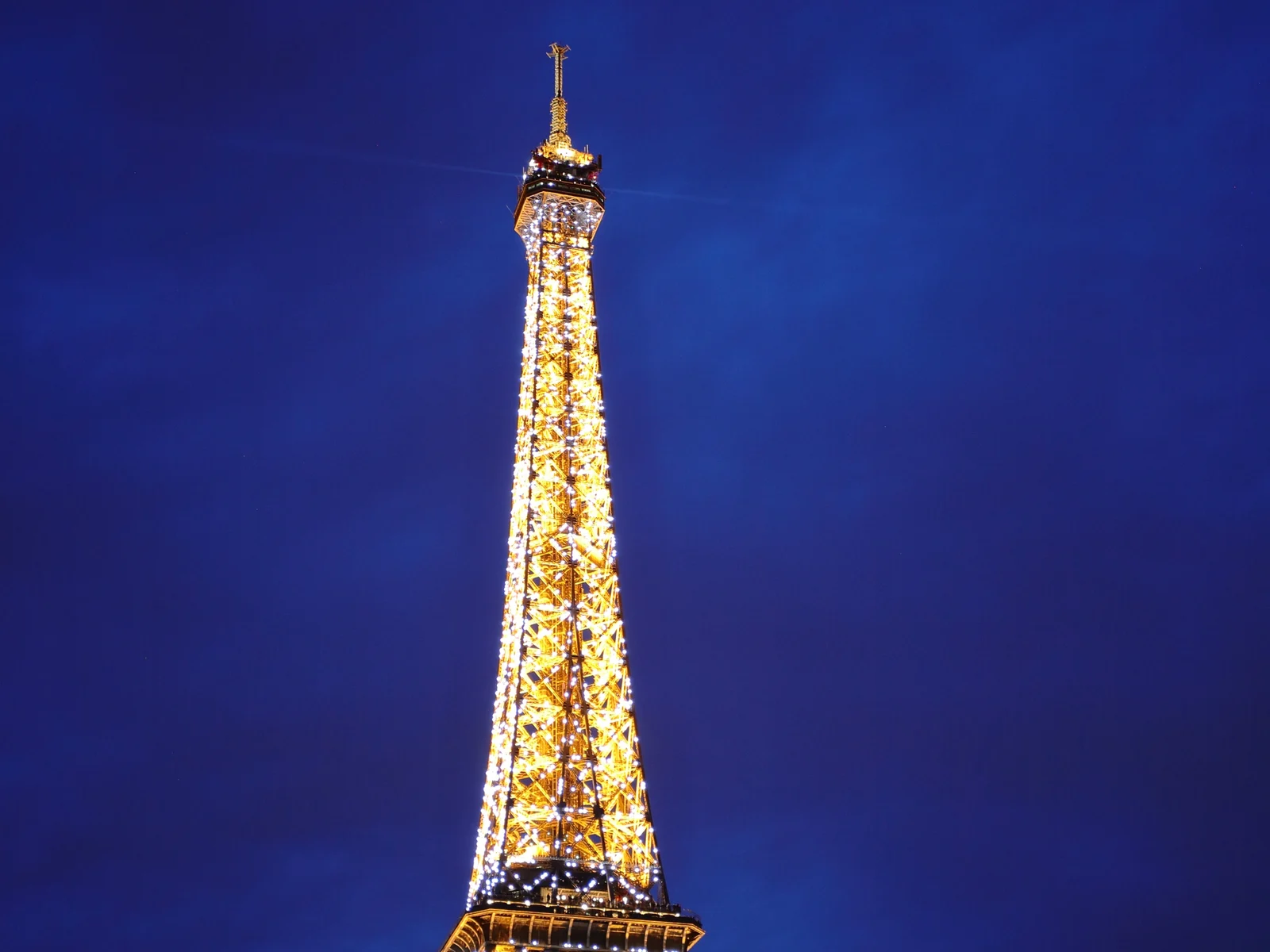 La tour Eiffel illuminée de ses scintillements dorés sur un ciel bleu nuit, à Paris