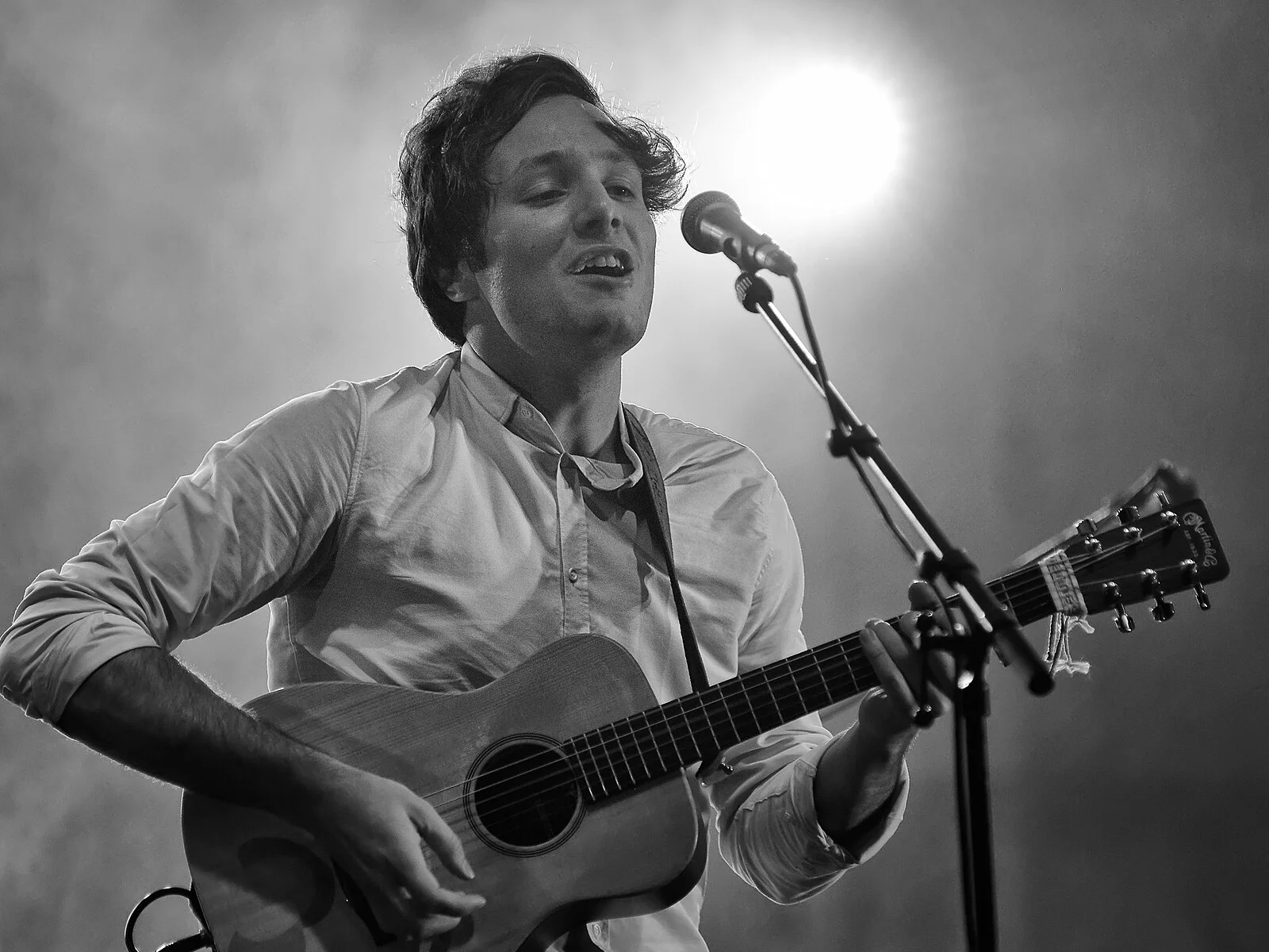 Portrait en noir et blanc de Vianney chantant et jouant de la guitare acoustique face à un micro, en 2015