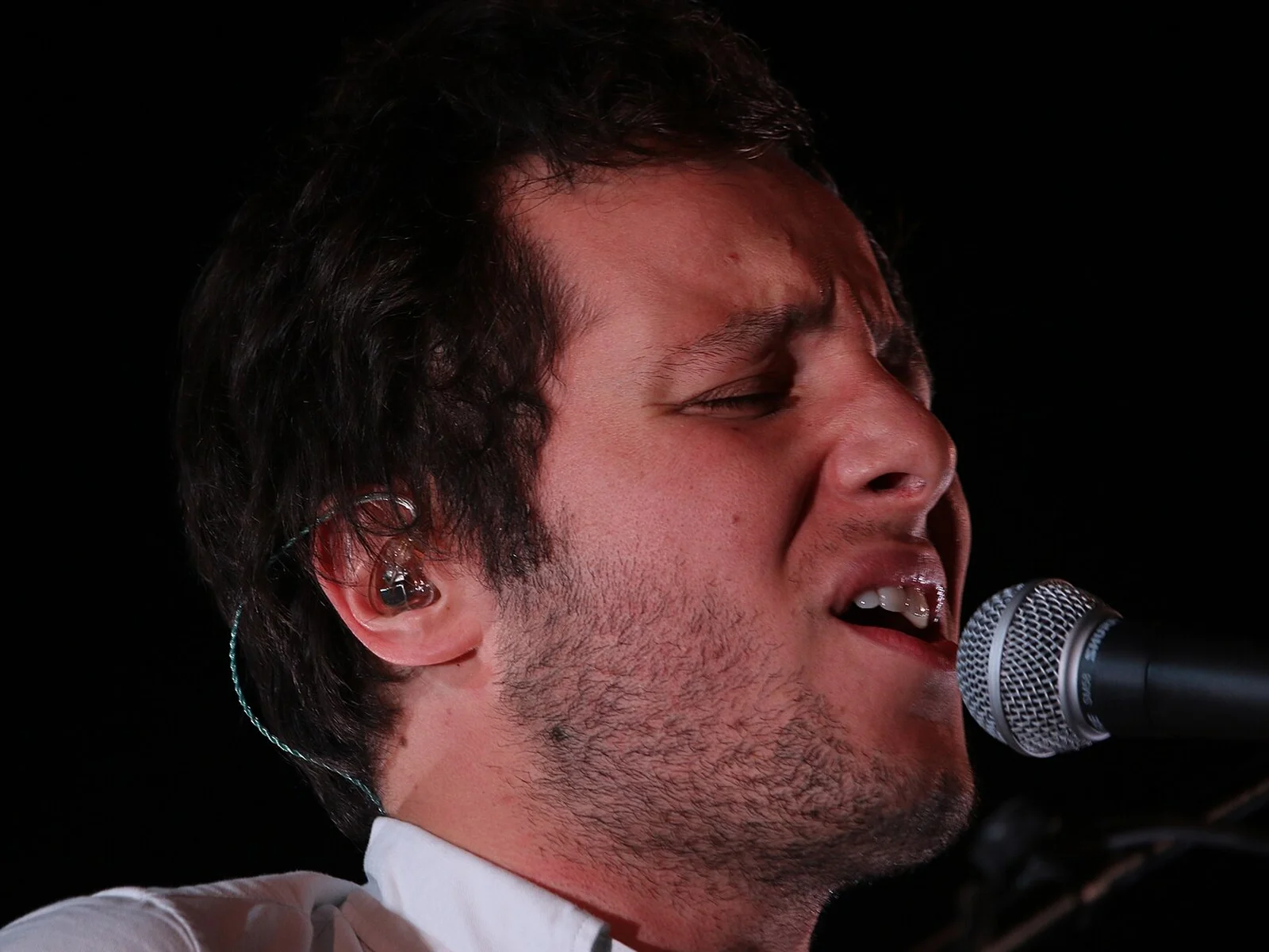 Gros plan sur le visage de Vianney qui chante, yeux fermés, devant un micro sur une scène sombre, Paléo 2016