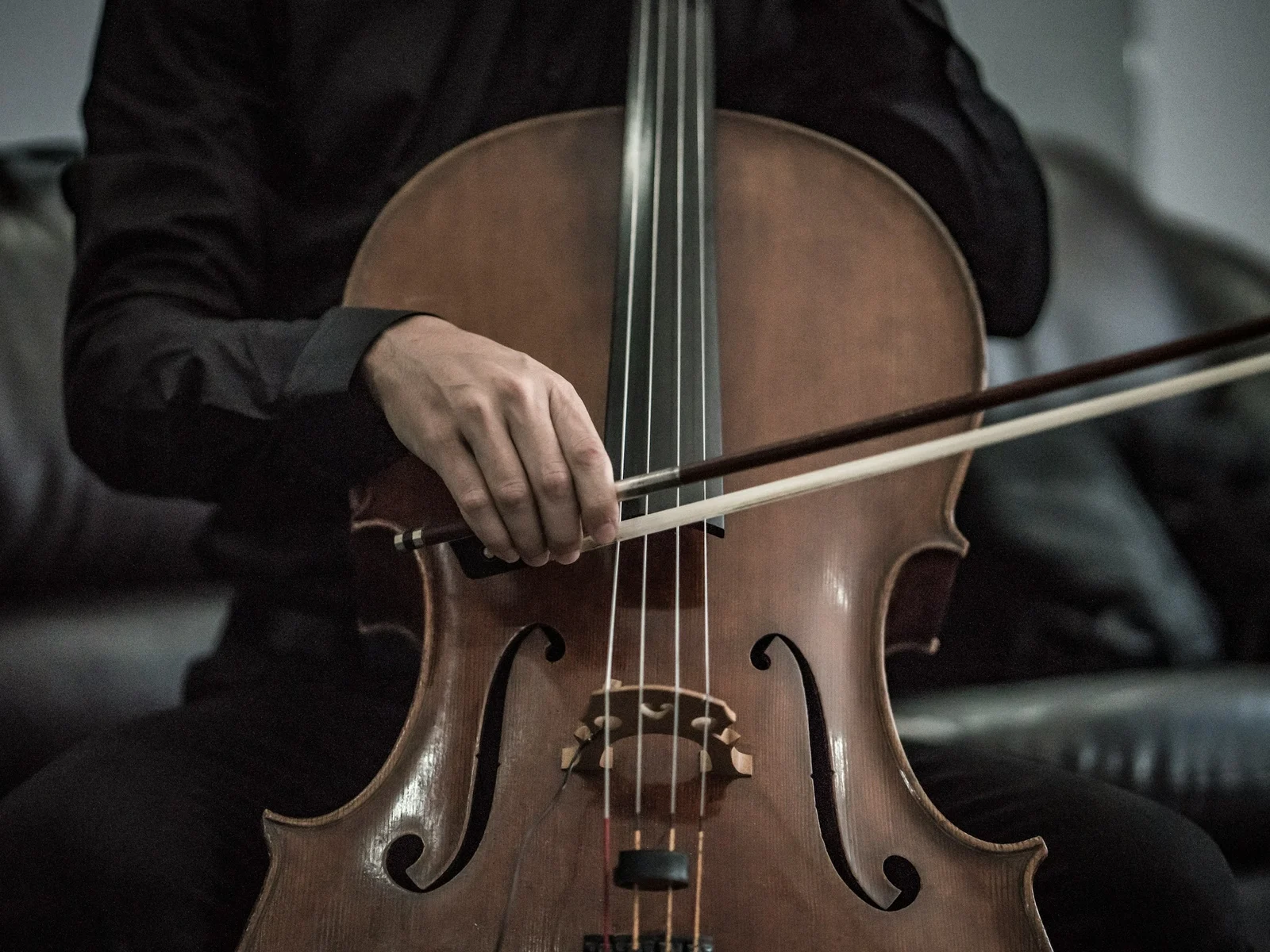Gros plan sur un violoncelle en bois sombre et la main d'un musicien en noir tenant l'archet, lumière douce de studio