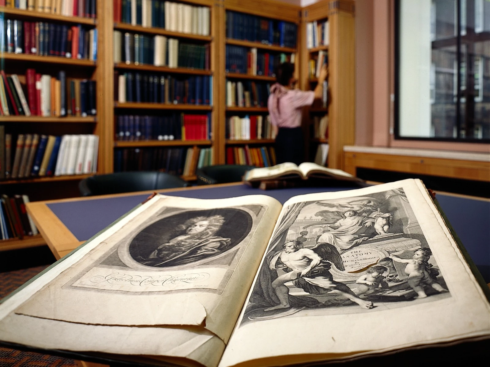 Livre ancien ouvert aux gravures historiques, avec des rayonnages de bibliothèque remplis de livres en arrière-plan